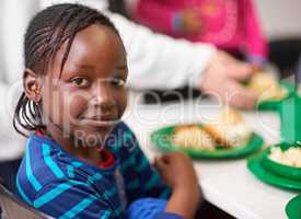 No child should be hungry. Portrait of a little girl sitting at a dining table with food provided by volunteers.