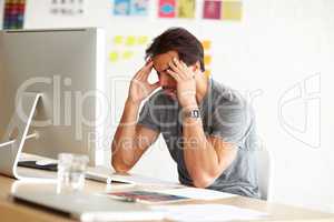 Exhaustion kills creativity. An overwhelmed man sitting at an office desk with his head rested against hands.