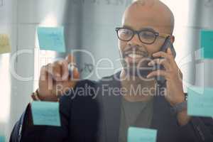 Your voice is my muse, babe. Shot of a young businessman talking on the phone while brainstorming on a glass wall.