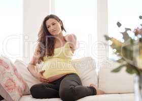 Feeling slightly uncomfortable. Shot of a young pregnant woman rubbing her neck.