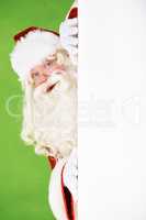 Peeping Santa. Santa peeking out around the corner of a white wall, on a green background - copyspace.