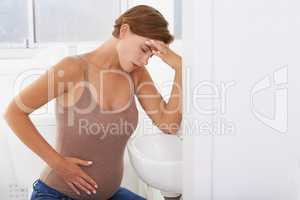 The aches and pains of pregnancy. A pregnant woman struggling with morning sickness in the bathroom.