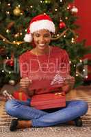 A special gift on Christmas day.... Shot of an attractive young woman sitting with a gift and reading a Christmas card.