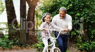 Shes got the hang of things. Shot of an adorable little girl being taught how to ride a bicycle by her grandfather at the park.