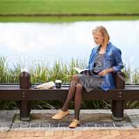 Enjoying a time-out in the park. Shot of an attractive blonde woman reading a book during her lunch break on a park bench.