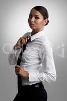 Straightening up her style. A beautiful young woman straightening her tie while looking at the camera.