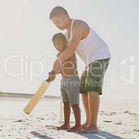 Raising a future cricket star. Shot of a father showing his son how to hold a cricket bat on the beach.