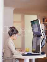 Shot of a young woman wearing smart glasses while working on a dual-screen computer. The commercial product(s) or designs displayed in this image represent simulations of a real product, and are changed or altered enough so that they are free of any copyr