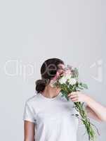 There is purity in flowers. Studio shot of an unrecognizable woman covering her face with flowers against a grey background.