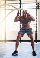 Building up some great results. Shot of a muscular young man working out with heavy ropes at the gym.