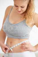 Achieving those weightloss goals. Curvaceous young woman measuring her waistline with a tape measure.