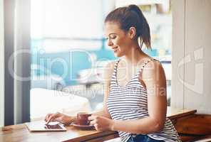 Coffee and wifi - the best way to spend the day. Shot of a young woman using her digital tablet in a coffee shop.