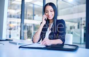 One signature gets it all. Shot of a young businesswoman going over paperwork and using a smartphone in a modern office.