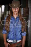 Being a cowgirl is who she is. An attractive young cowgirl standing in the stables.