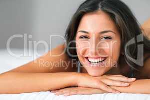 Im keeping this smile for the rest of the day. Shot of a beautiful young woman relaxing on her bed.