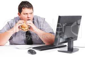 Stop showing me healthy things. A young man eating his lunch at his desk at work while staring with mouth agape at his monitor - unhealthy eating habits.