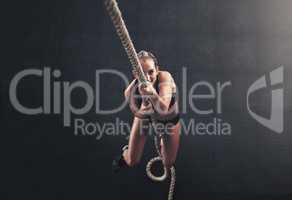 Hold on tight through your challenges. Shot of a sporty young woman climbing a rope in a gym.