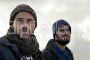 Wrapped up against the crisp ocean chill. Two handsome young fishermen standing on the beach on a cool morning.