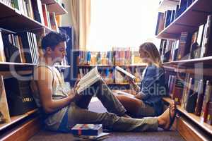 Studying together, but separately. Two students reading separate textbooks in the library.