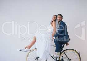 Arrive in style. Studio shot of a newly married young couple riding a bicycle together against a gray background.