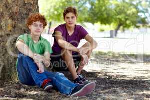 Catching some shade on a hot day. Shot of two teenage boys relaxing in the shade of a tree at the park.