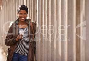 Got my coffee, ready to go. A portrait of a beautiful young woman leaning against a concrete wall in the city.