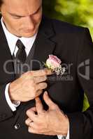 Last minutes preparations. Handsome young groom adjusting his boutonniere.