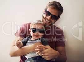 Coolness runs in this family. A young father and his infant son wearing matching sunglasses and laughing.