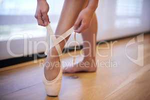 Adjusting perfection. Closeup of a woman in a satin ballet shoe with hands tying the ribbon.