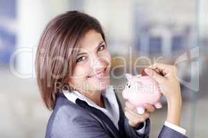 Every little bit counts. Portrait of an attractive businesswoman putting a coin into a piggybank.