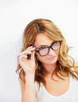Cute glance. A pretty young woman looking over her glasses at you while isolated on white.