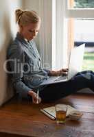 Relaxed afternoon. A young woman sitting on a floor doing some researching on her laptop.