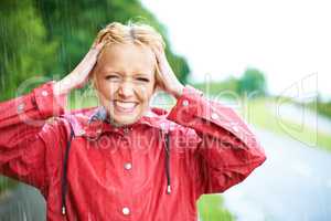 Nothings better than a little fresh rain water. Gorgeous young blonde woman wearing a red raincoat in the rain outdoors on a country road.