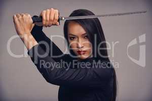 The way of the ninja. Studio portrait of a beautiful young woman in a martial arts outfit wielding a samurai sword.