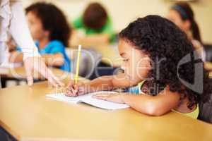 Fantastic work. A cute little girl smiling as she does her homework in class.