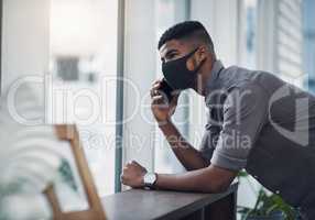 Business goes on, as long as we keep safe. Shot of a young businessman wearing a face mask while talking on a cellphone in an office.