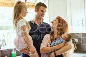 All together in the kitchen. Shot of a cheerful young family grouped together while standing inside the kitchen at home.