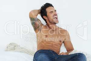 Early riser. Shot of a bare-chested young man sitting on his bed and yawning.