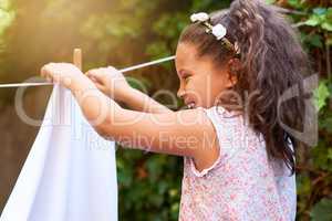 Shes full of laughter. Shot of a young girl hanging up laundry on a washing line.