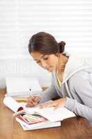 Taking down spark notes. Side view of a young college student taking notes from her textbook.