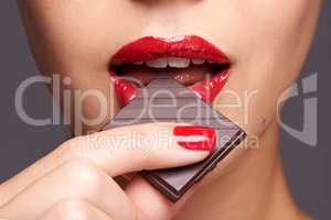Every woman needs a guilt-free chocolate day. Closeup portrait of a cute young female biting on a chocolate bar.