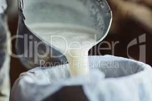 The steps to making cheese. Cropped shot of an unrecognizable male farmer pouring unprocessed milk into a container inside a barn.