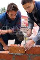 Showing the young one how its done. Shot of bricklayers at work.