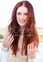 Her beauty brightens up the landscape. A beautiful young redheaded woman smiling at the camera.