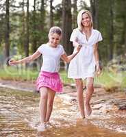 Lets go this way mom. A cute little girl running through a wilderness stream with her mother.