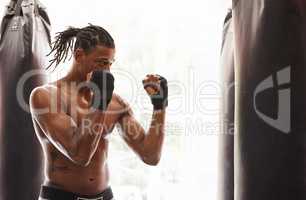 Fighting prowess. Shot of a young boxer practicing on a punching bag in a gym.