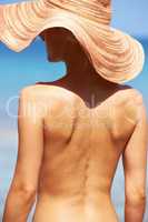 Bare and beautiful. Rear view of topless young woman in sun hat standing and tanning.