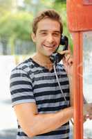 Sharing his adventures - calling home. A handsome young man smiling and having a conversation on a public telephone.