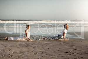 The ambience of the area will add to your yoga. Shot of a young couple practising yoga together on the beach.