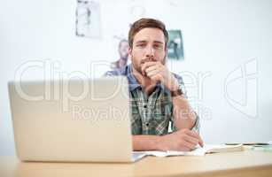 Portrait of a casually-dressed young man using a digital tablet at his desk. The commercial designs displayed in this image represent a simulation of a real product and have been changed or altered enough by our team of retouching and design specialists s